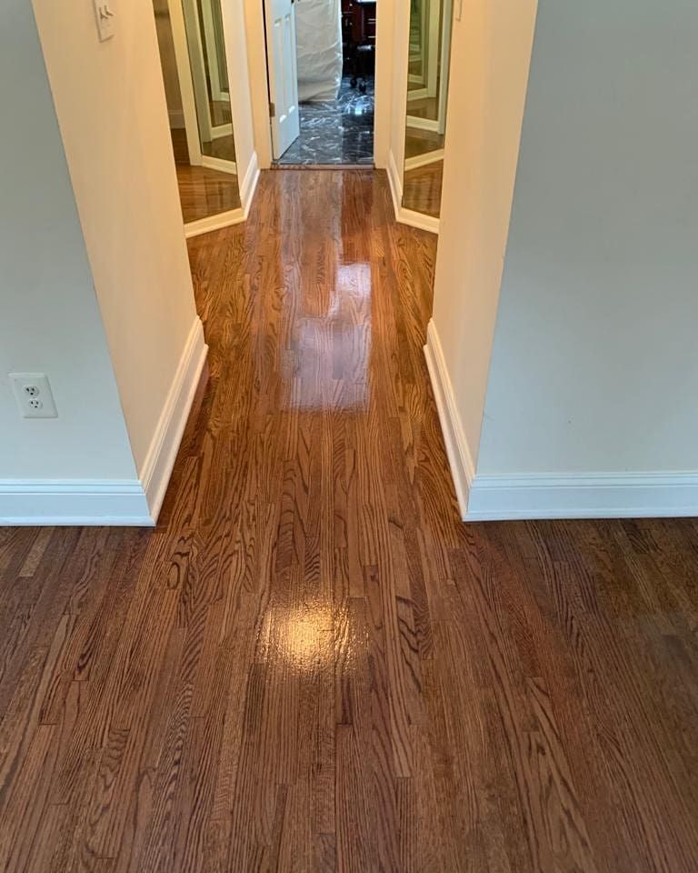 Hallway with shiny, dark wood floor. Light beige walls, white baseboards, mirrors at the end.