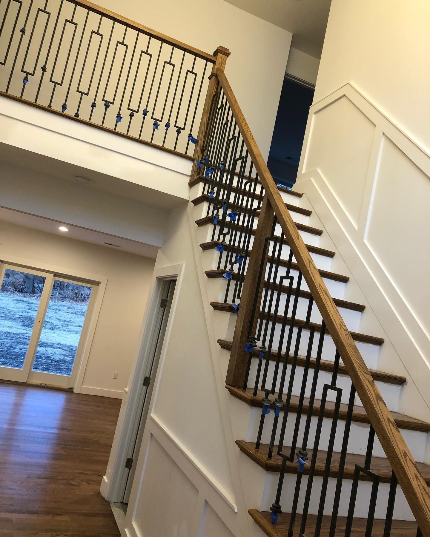 Wooden staircase with black metal balusters and white walls.