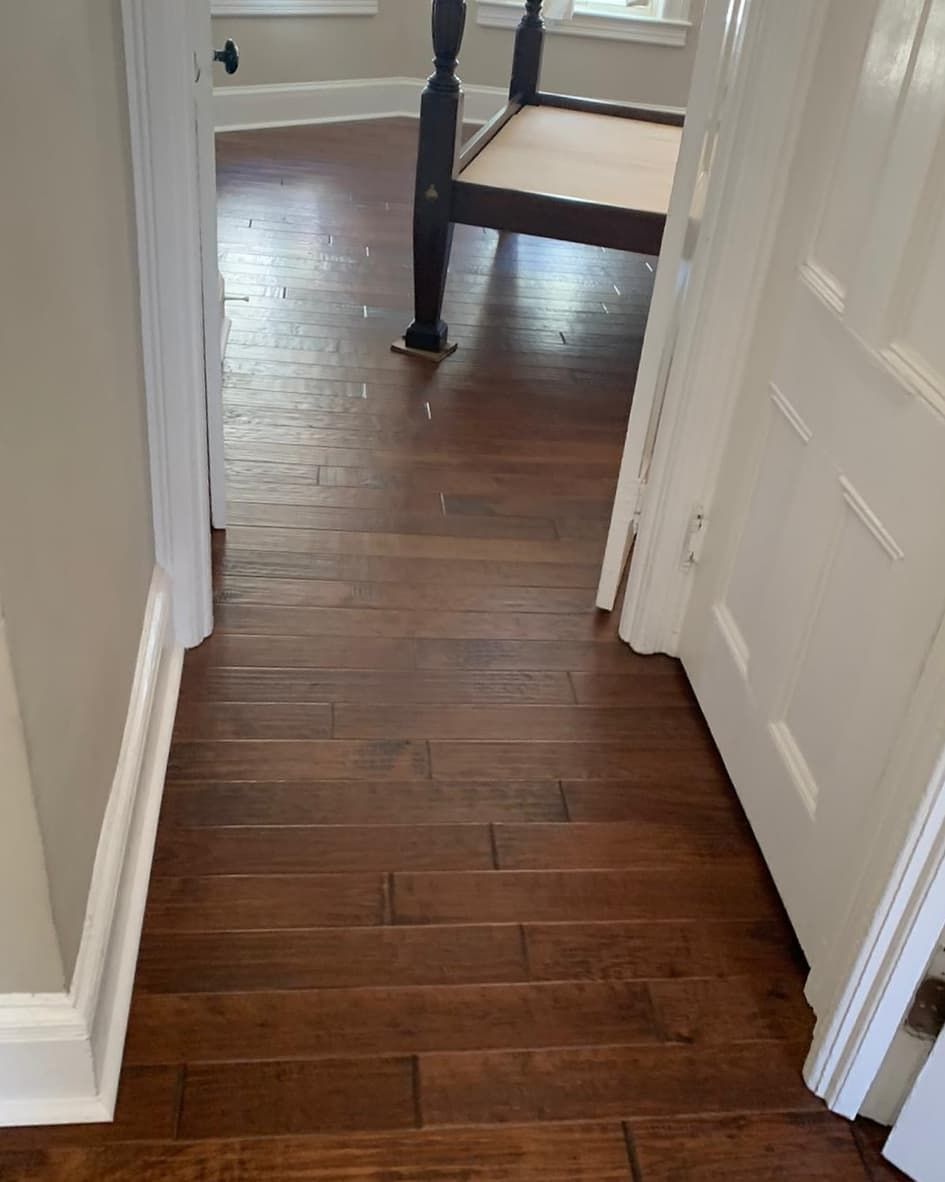 Dark wood floor in hallway leading to a bedroom with a bed. White trim and door frame.