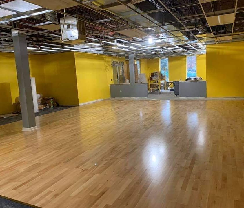 Large room with yellow walls, hardwood floor, and exposed ceiling. Construction materials visible.