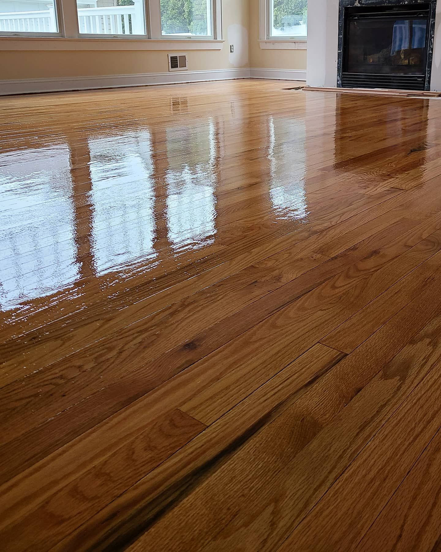 Newly finished hardwood floor reflecting sunlight from windows in a room with a fireplace.