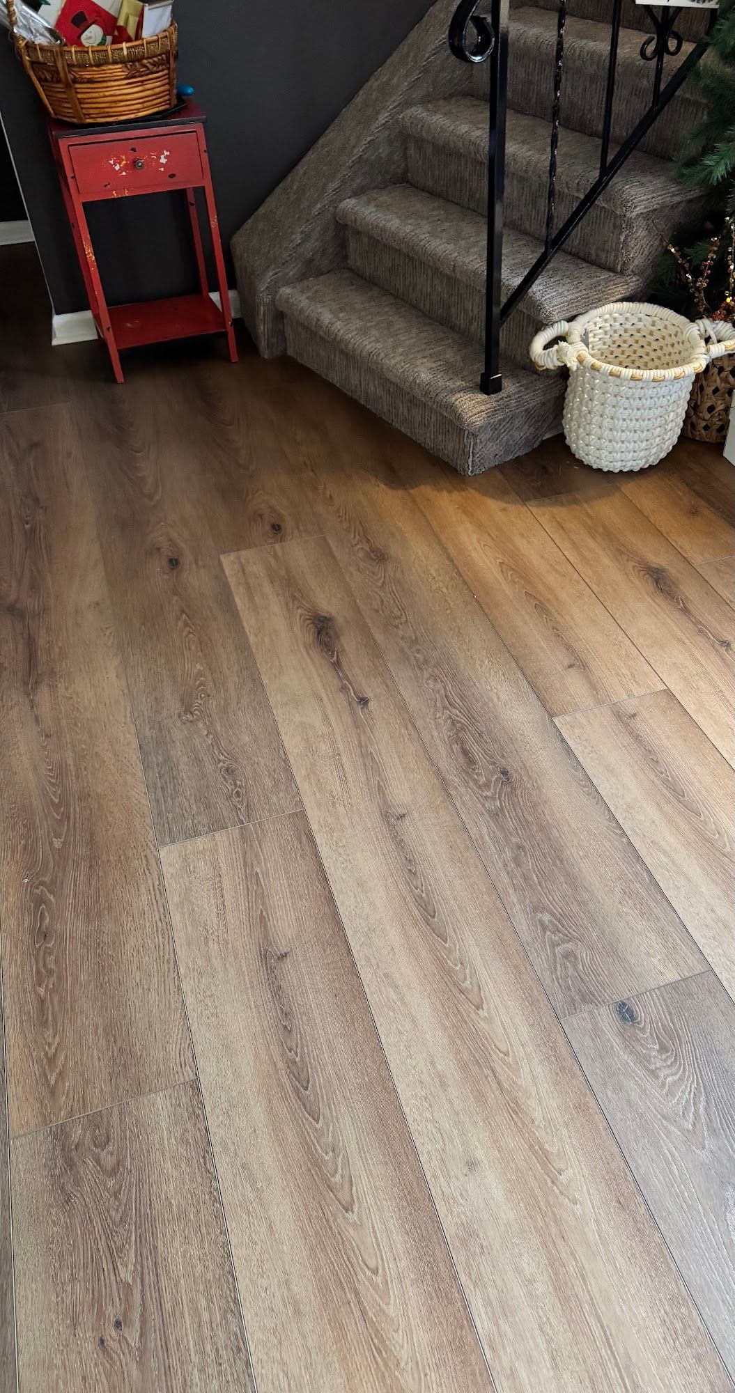 Wooden-look flooring with a staircase. A red side table and basket are in the upper left corner. A white basket sits 