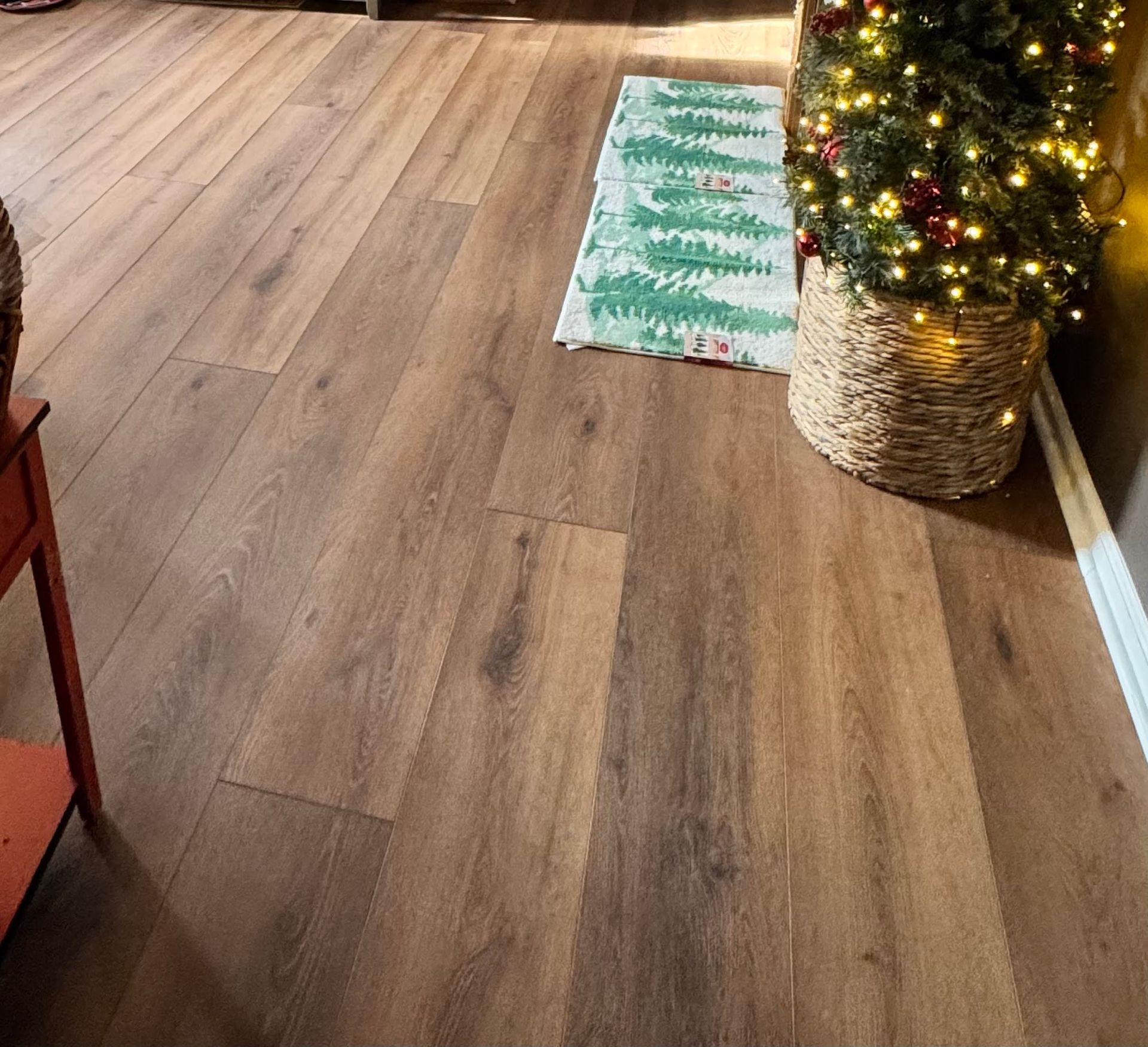 Wooden floor with a small Christmas tree in a woven basket and a holiday rug.