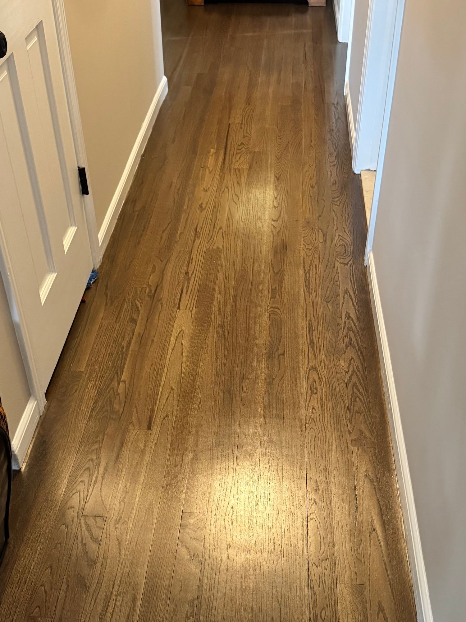 Wooden hallway with a brown floor, white trim, and beige walls.