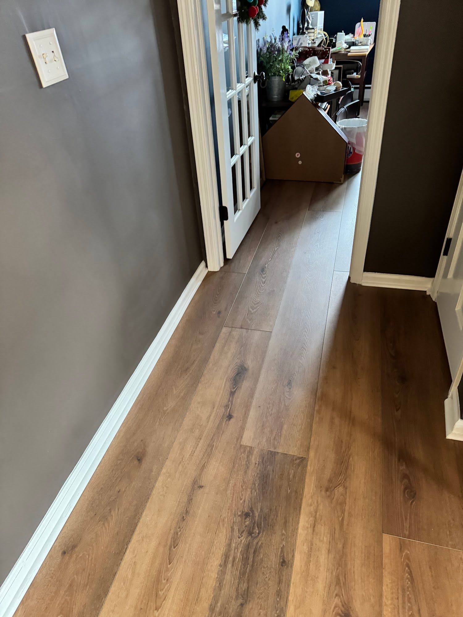 Brown wood-look flooring in a hallway with dark gray walls and a partially open door.