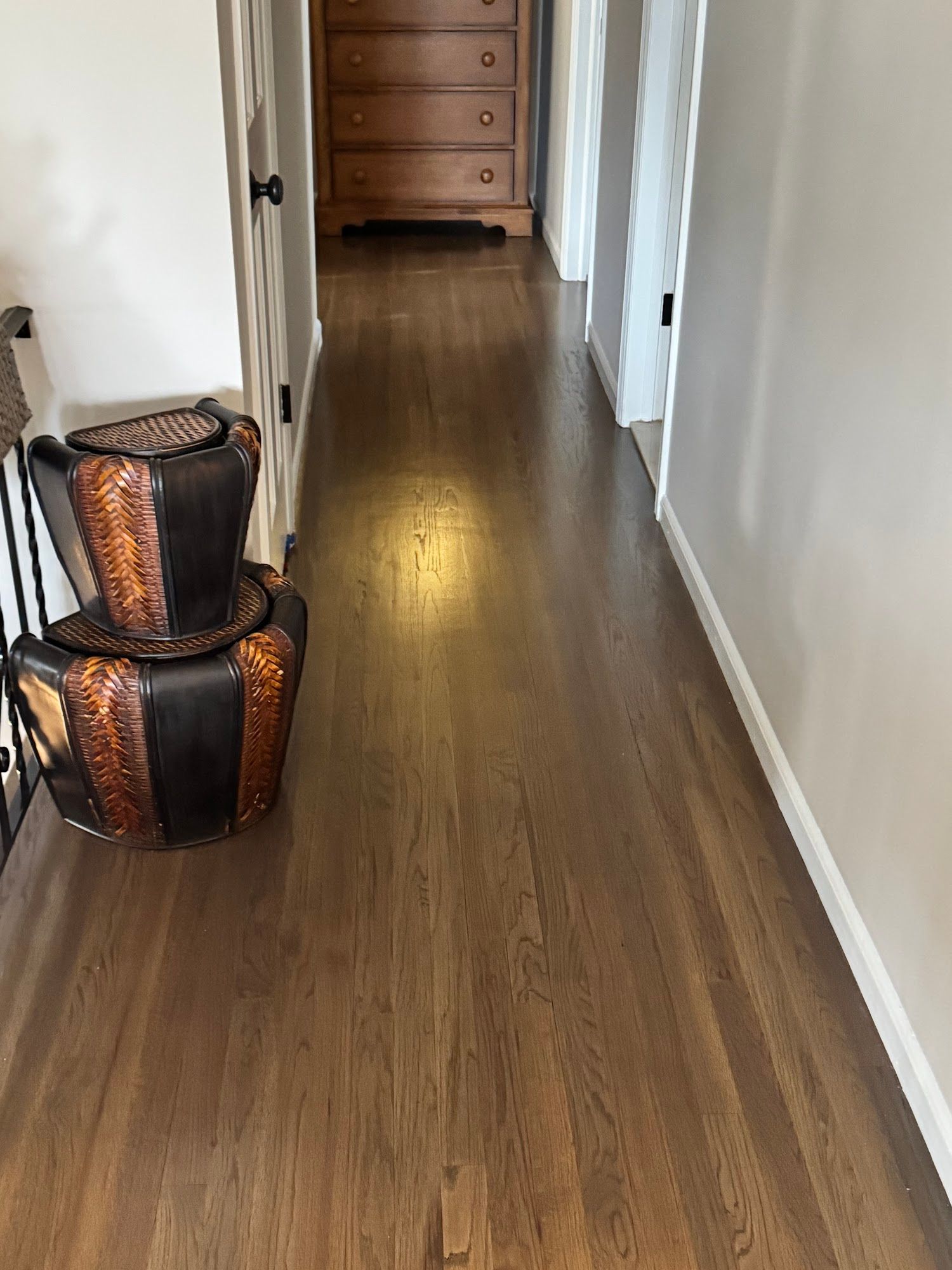 Hallway with brown hardwood floor, white walls, and a wooden chest of drawers at the end.
