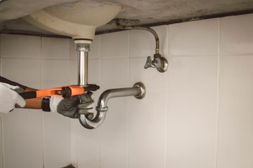 Plumber using a wrench to tighten sink drain pipes under a bathroom sink