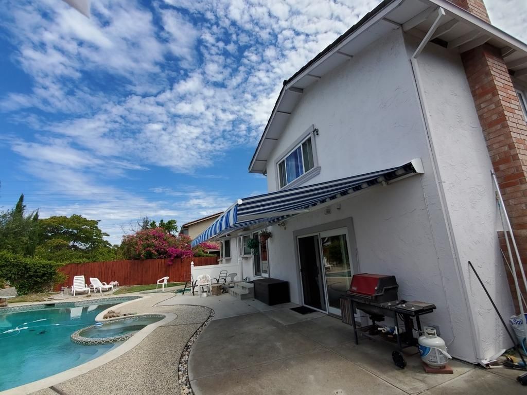 A white house with a blue and white awning over a swimming pool