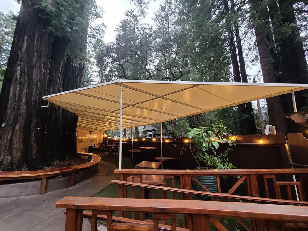 A picnic area with tables and benches under an umbrella in the woods.