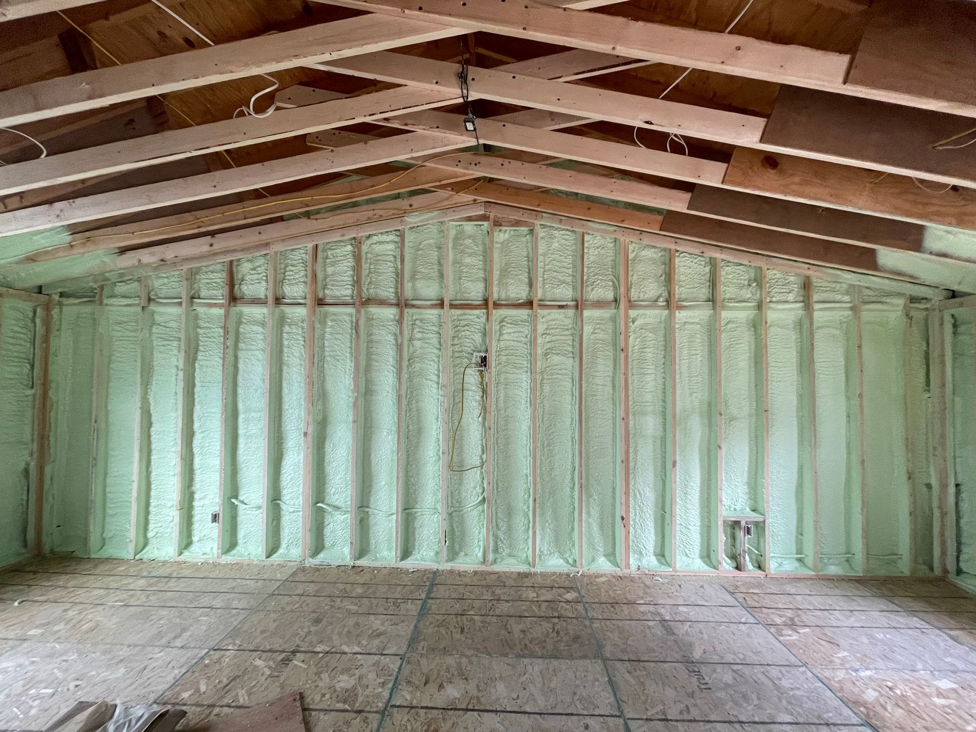 Empty unfinished room with exposed roof beams, pale green insulated walls, and a concrete floor.
