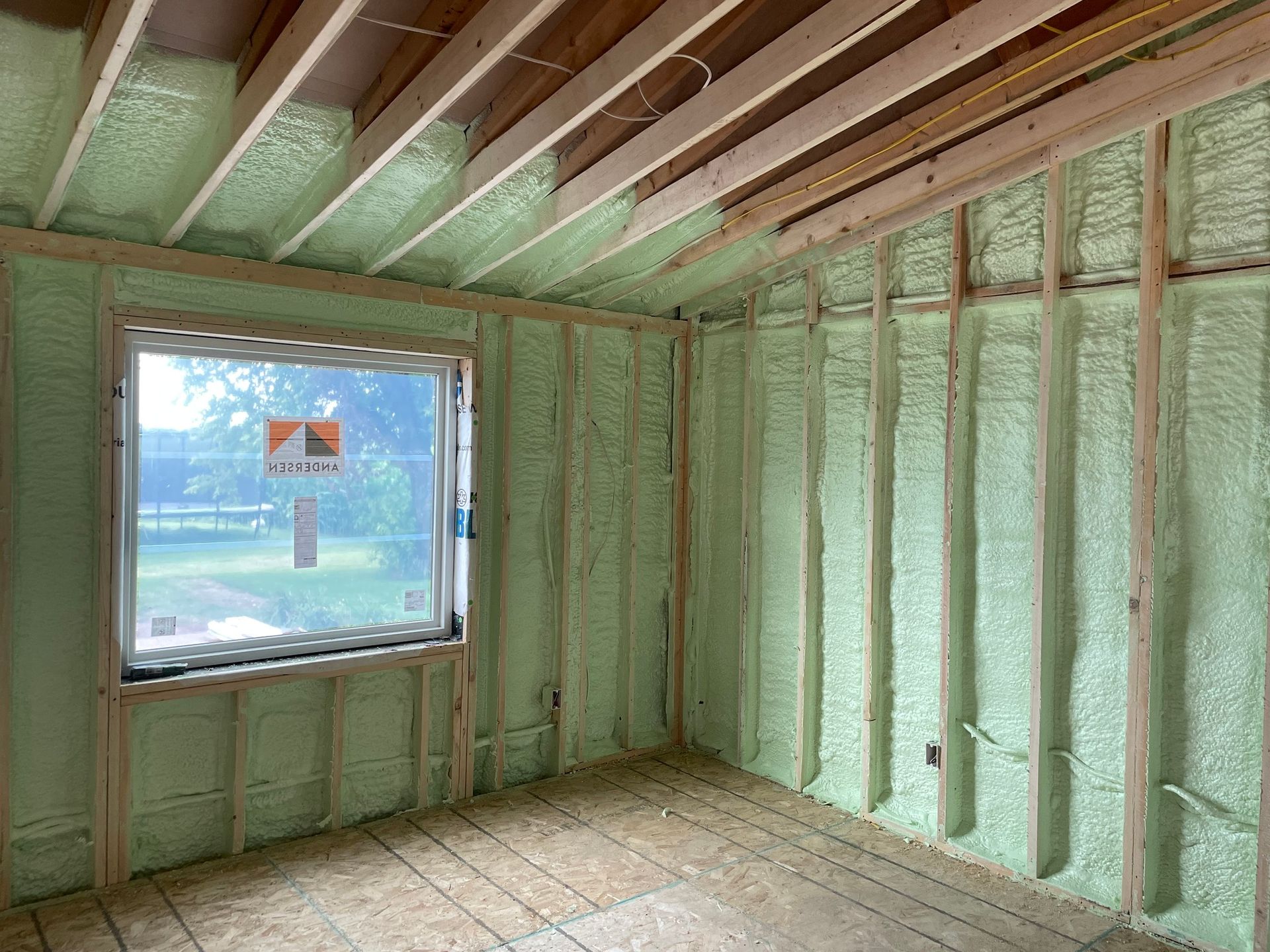 Insulated unfinished room with green spray foam on walls, exposed ceiling joists, and a window opening.