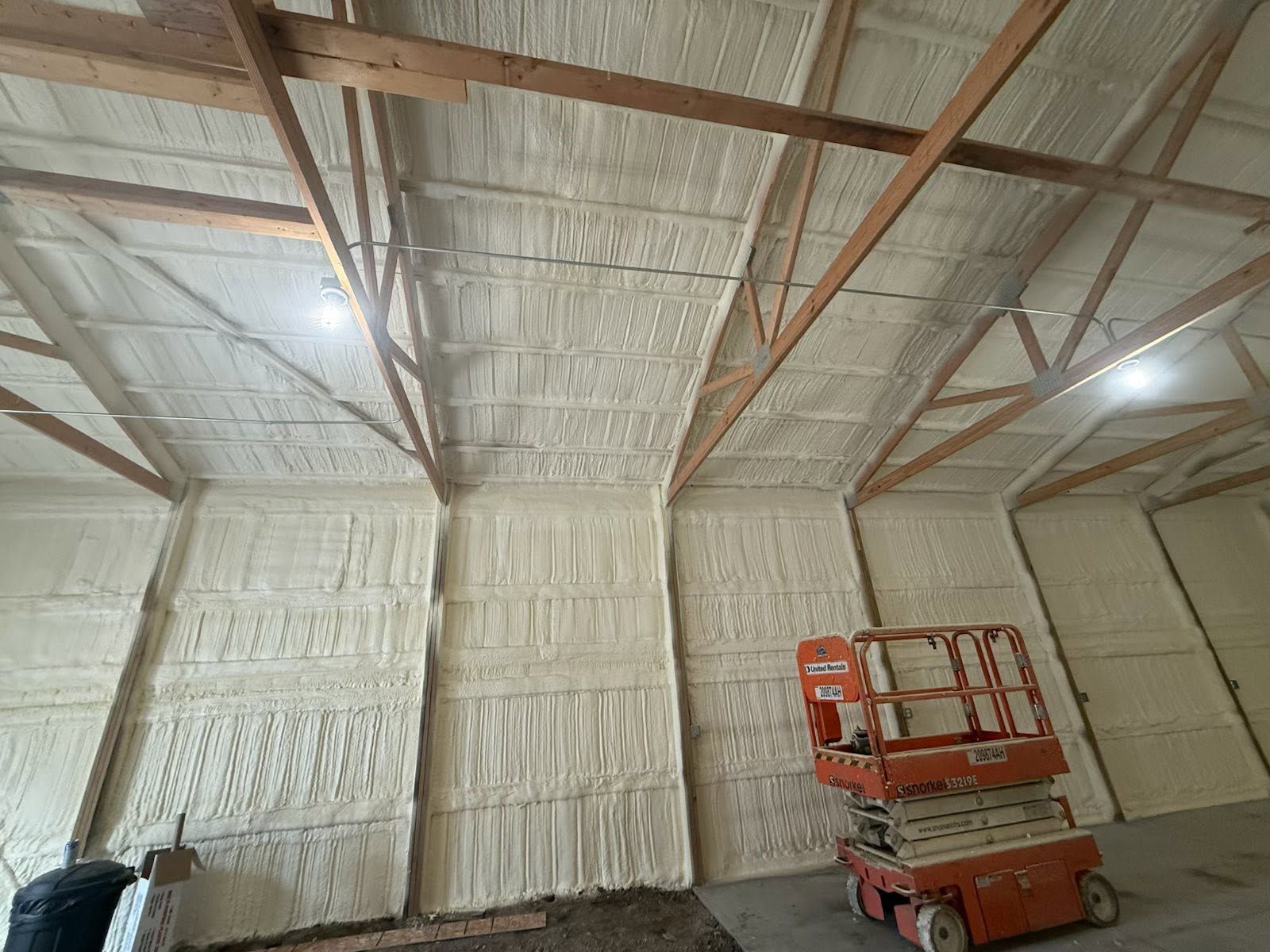 Insulated warehouse interior with exposed beams and a red scissor lift near the right wall