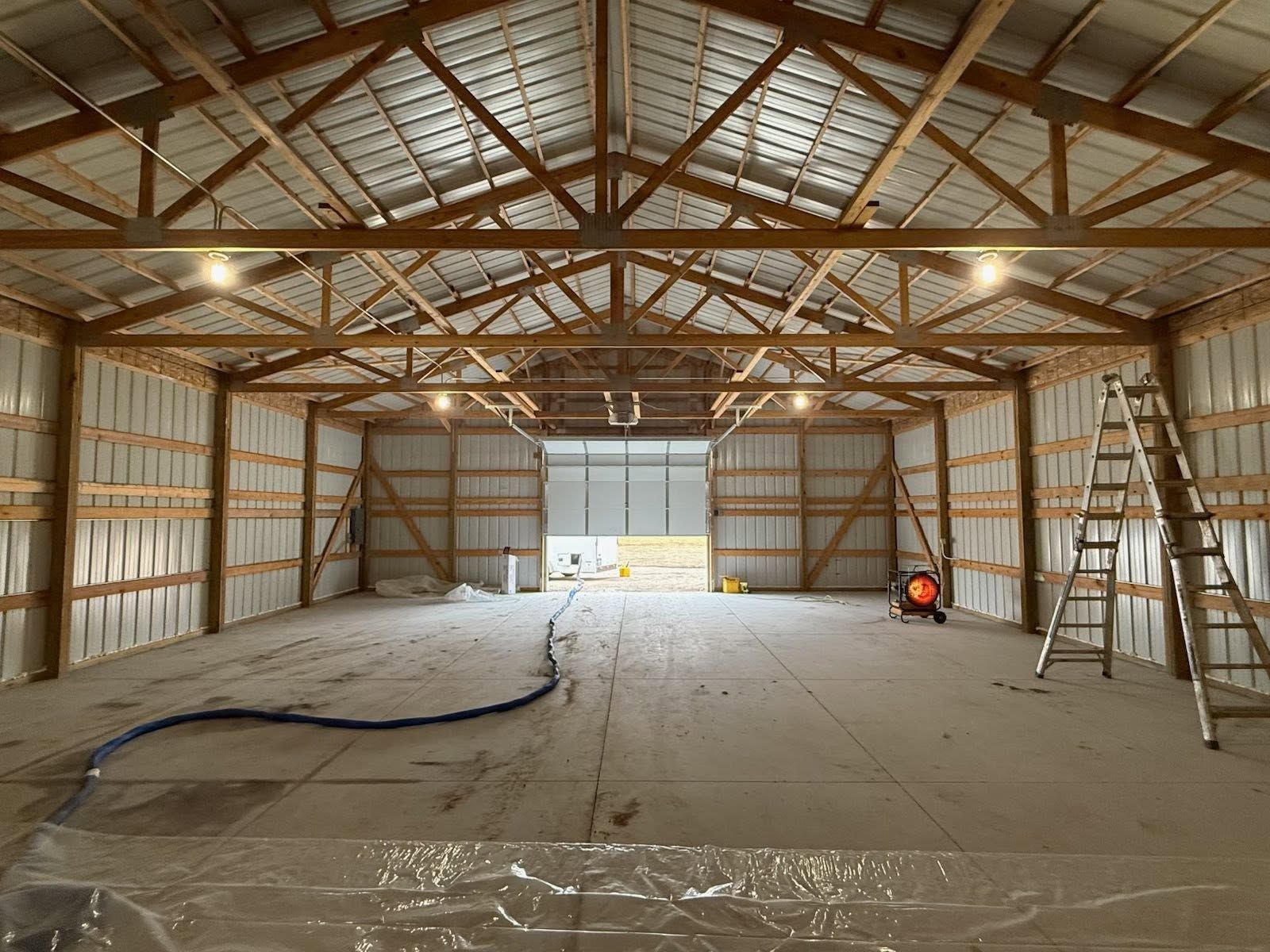 Interior of a metal barn under construction, with exposed beams, ladder, and equipment on the floor