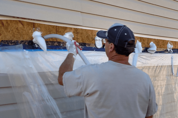 Worker applying house wrap over plastic sheeting on a home exterior wall