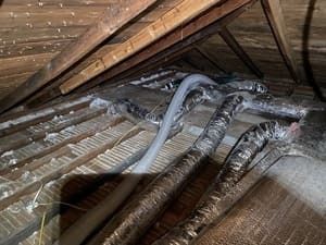 Attic with exposed insulation and several air ducts running along the roof rafters