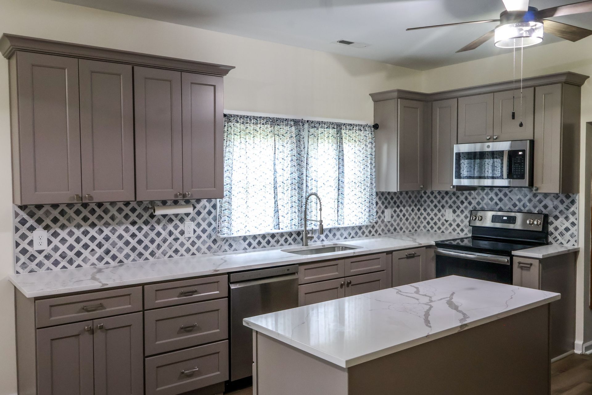 Gray kitchen with white countertops, blue and white backsplash, and a kitchen island.