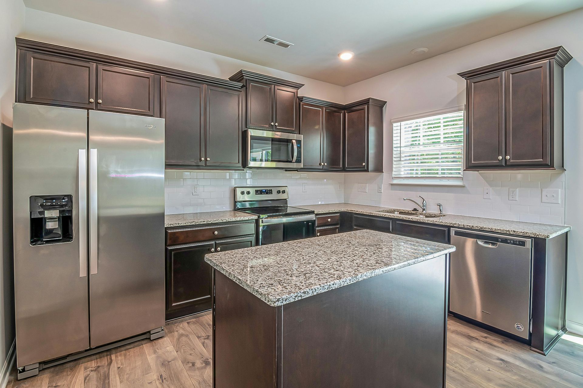 Modern kitchen with stainless steel appliances, dark cabinets, and a granite island countertop