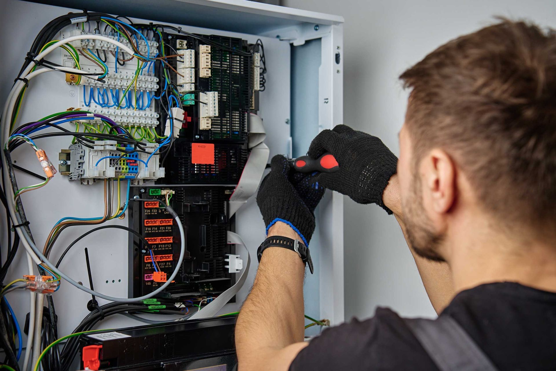 Technician wiring an electrical control panel with a screwdriver inside an open cabinet