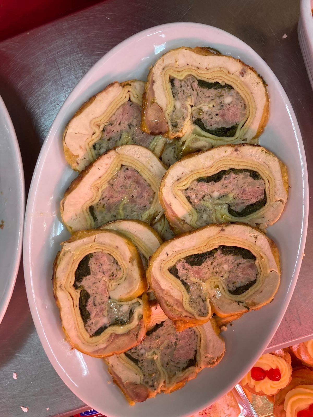 Su un piatto bianco sono disposte diverse fette di involtino di carne, che mostrano uno strato a spirale di carne cotta e verdure.