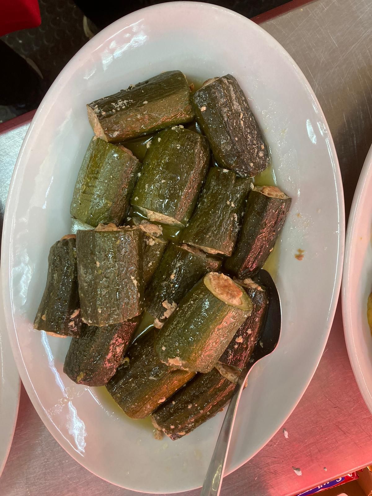 Un piatto ovale bianco colmo di mezze zucchine verdi cotte e ripiene, condite con una salsa leggera.