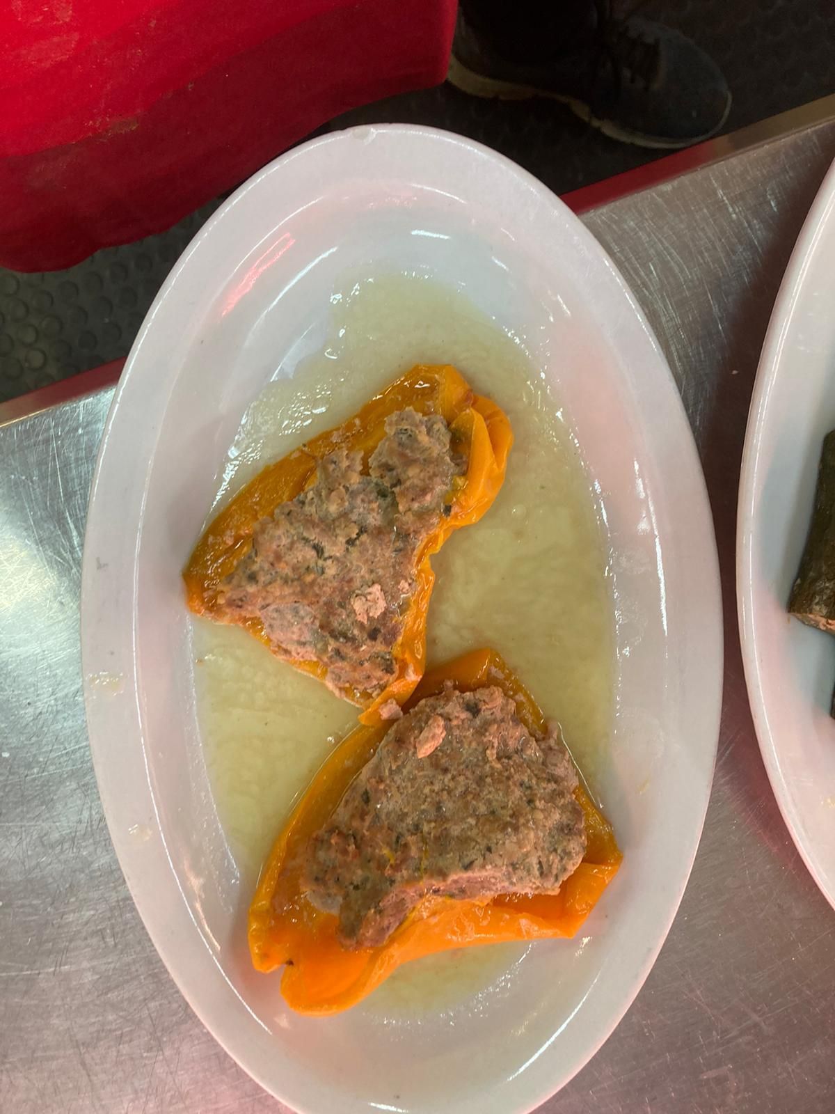 Due metà di peperone arancione ripiene di carne, adagiate in un brodo chiaro su un piatto ovale bianco.