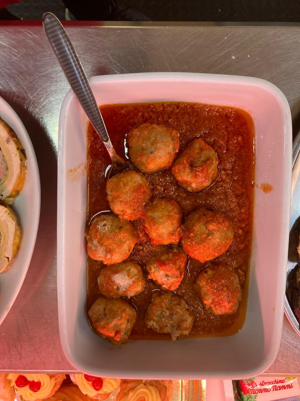 Un piatto rettangolare bianco, ripieno di polpette cotte in salsa di pomodoro rossa, appoggiato su un piano di lavoro metallico.