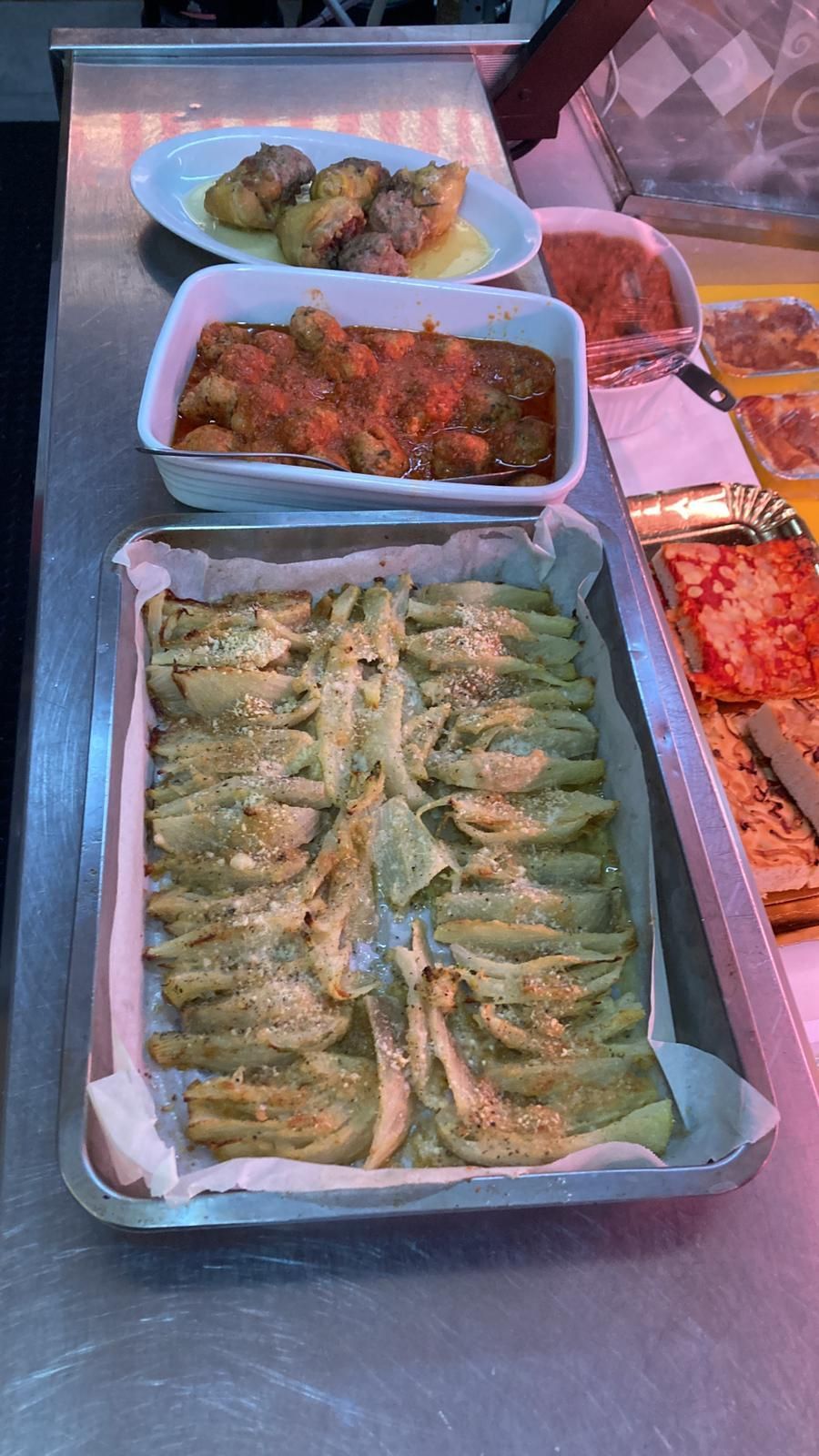 Un bancone in acciaio inossidabile espone piatti preparati, tra cui verdure verdi ripiene, carne in umido e pane piatto al forno.