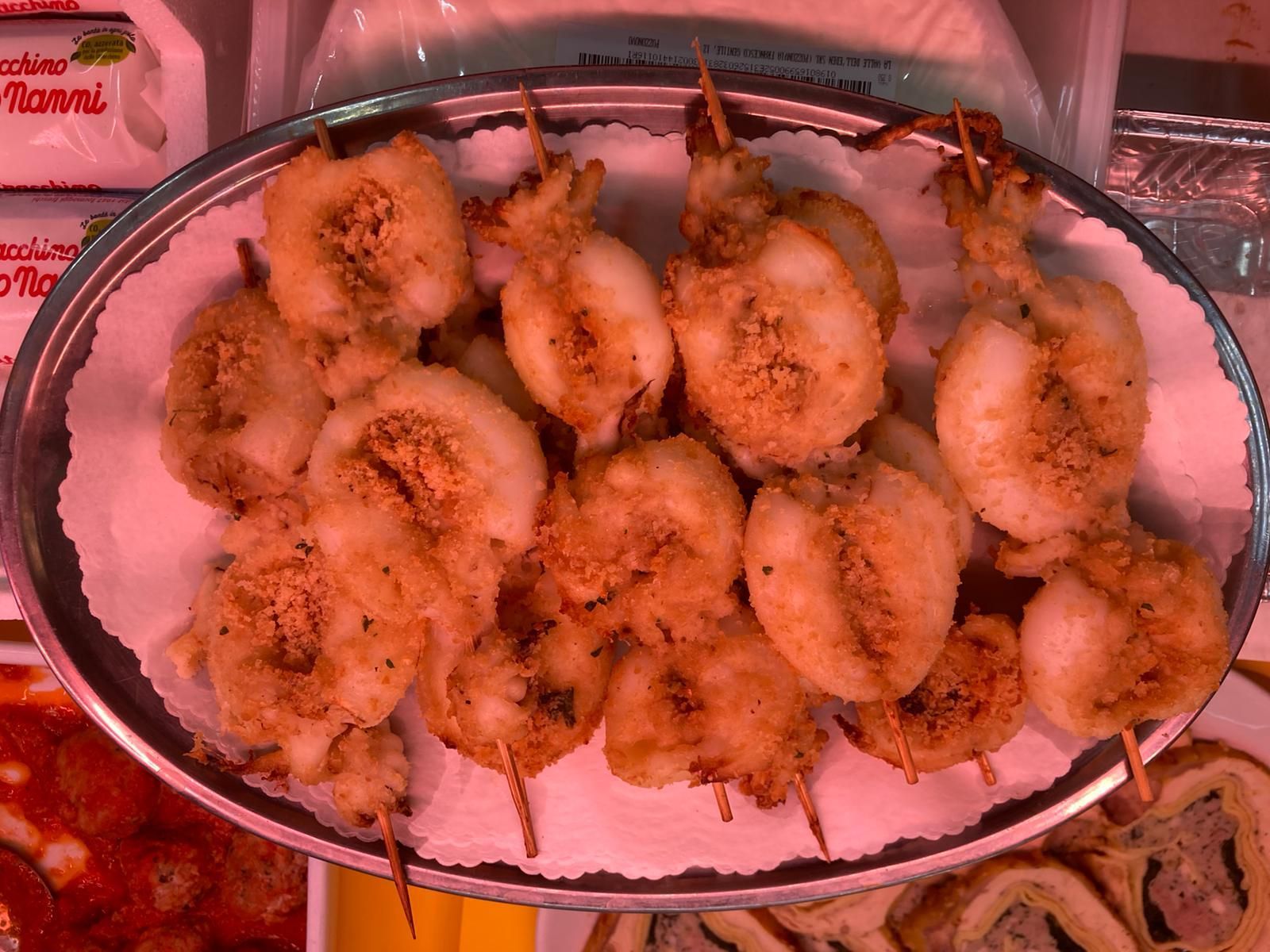 Un vassoio d'argento contenente diversi spiedini di gamberi fritti, dorati e impanati, adagiati su carta da forno bianca.