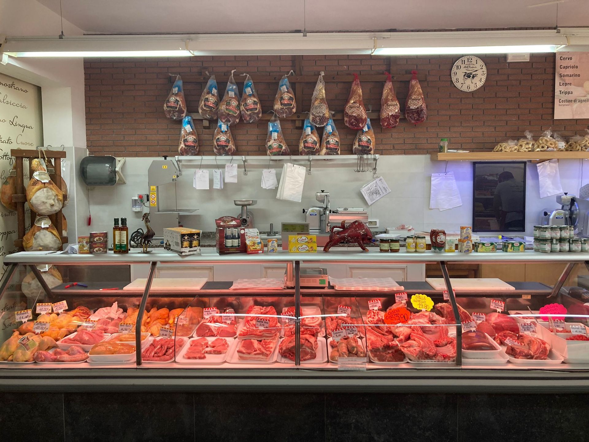 Una vetrina di macelleria piena di vari tagli di carne cruda, con salumi appesi alla parete dietro il bancone.