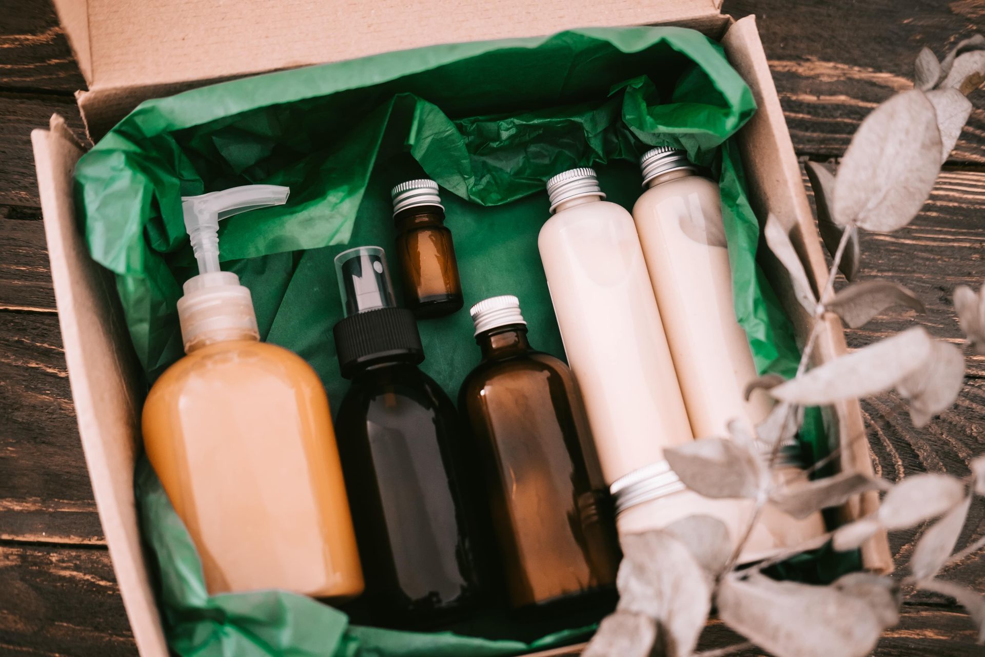 Box of beauty products on green tissue paper. Includes bottles and a pump dispenser.