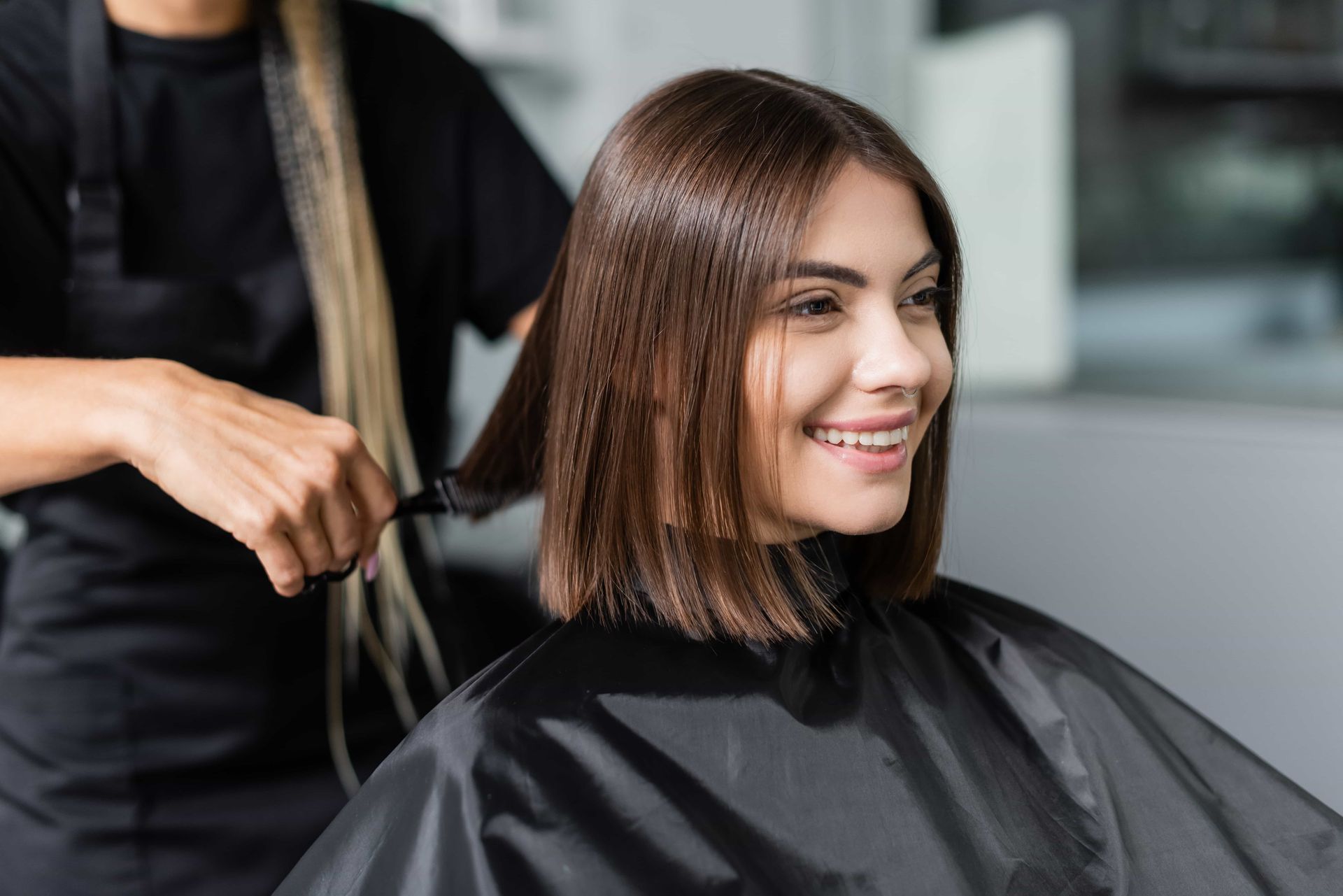 Woman getting a haircut, smiling, in a salon. Stylist is trimming hair with scissors.