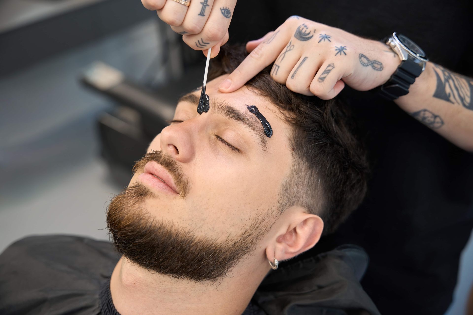 Man having eyebrow waxing treatment in a salon; applicator in use.