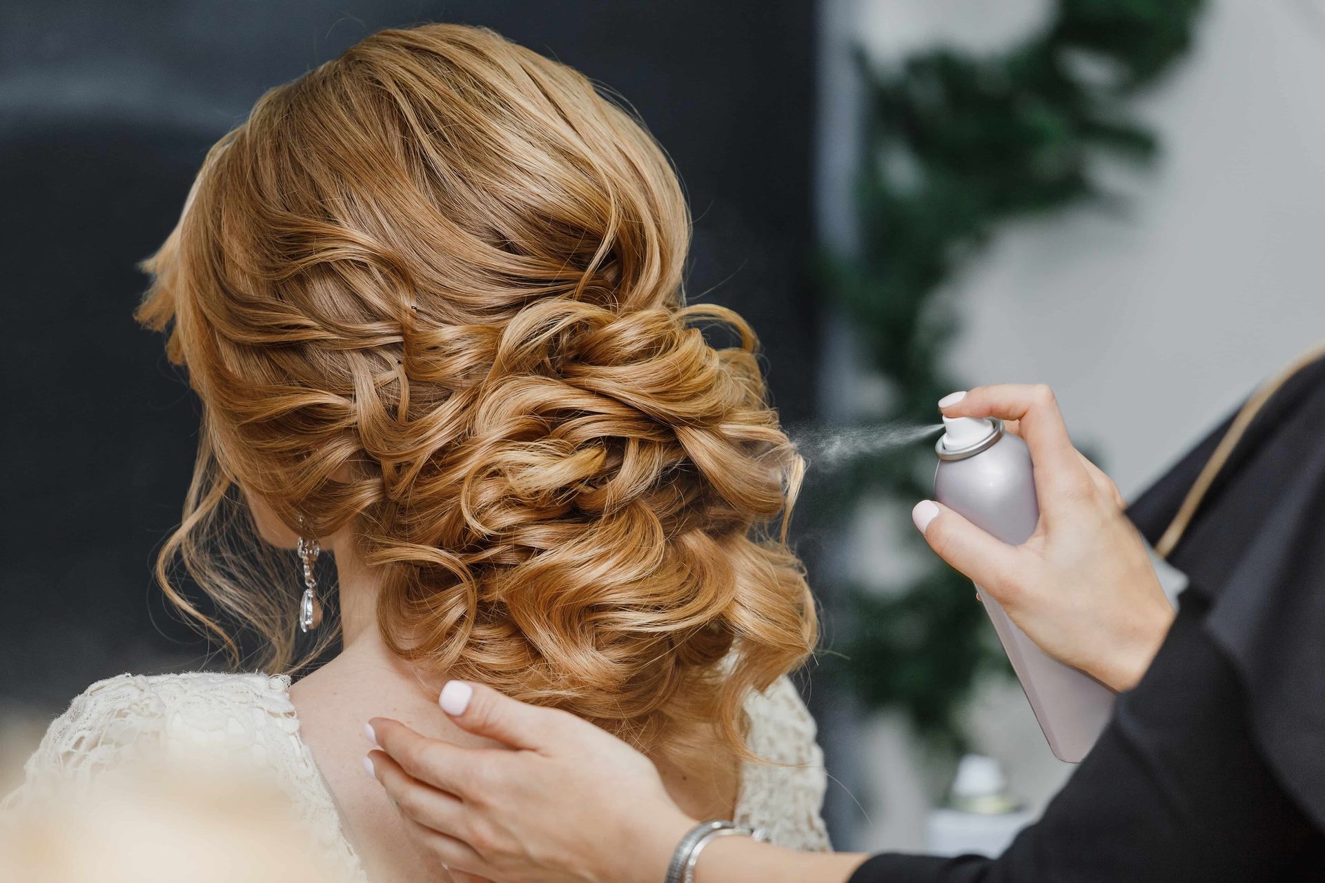 Hair stylist sprays hairspray on an updo hairstyle at a salon.