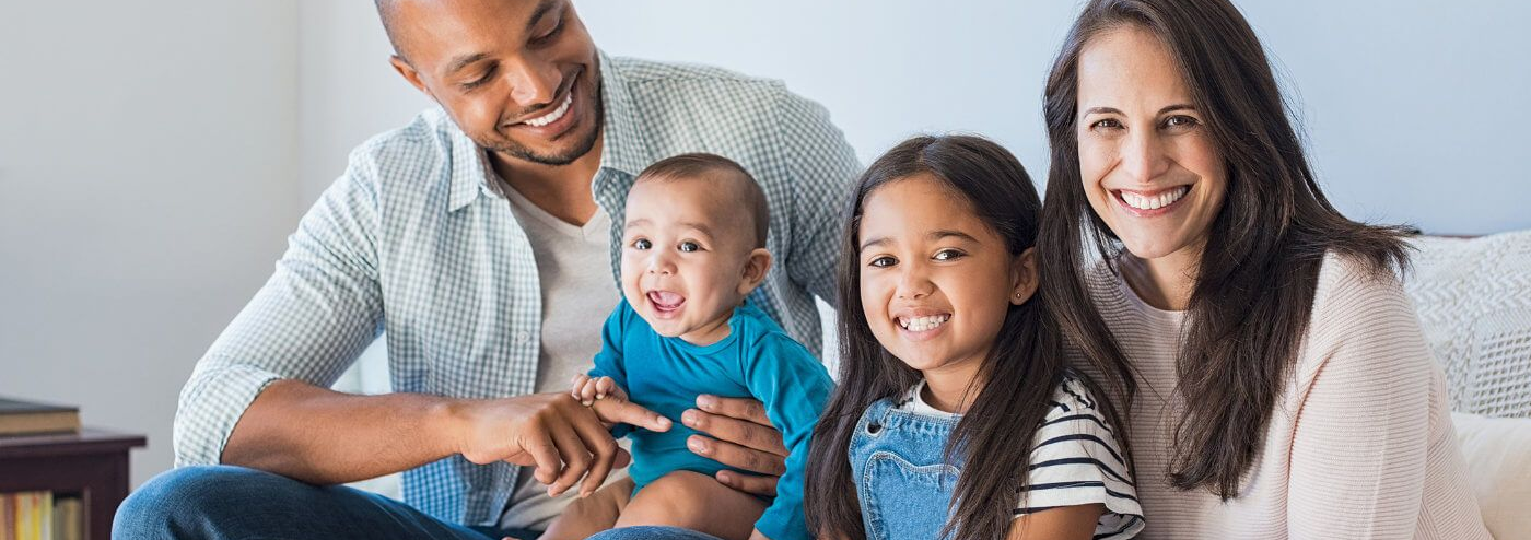A family is sitting on a couch with a baby and two children.