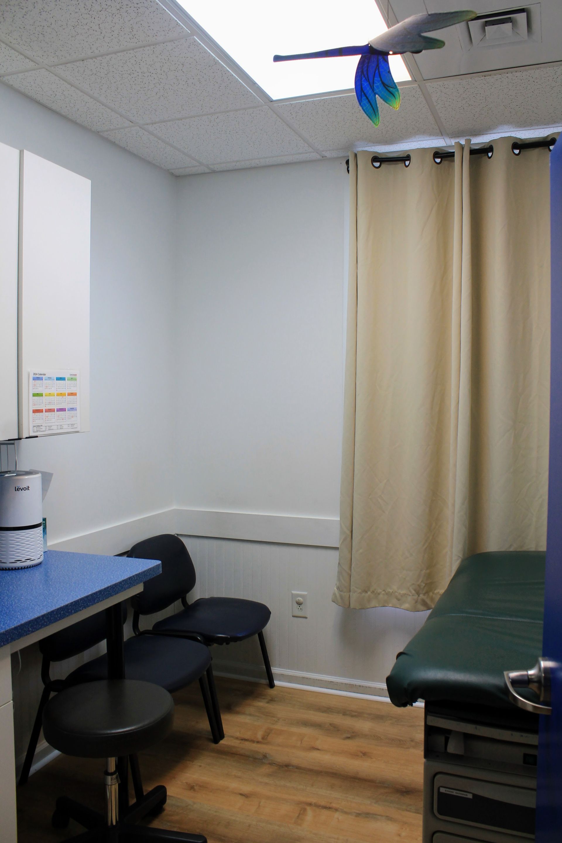 A doctor 's office exam room with table, chairs and window
