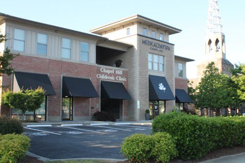 A large brick building with black awnings and a church in the background.