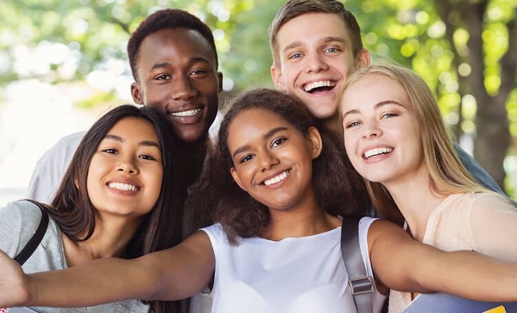 Group of smiling teens taking a selfie outdoors.