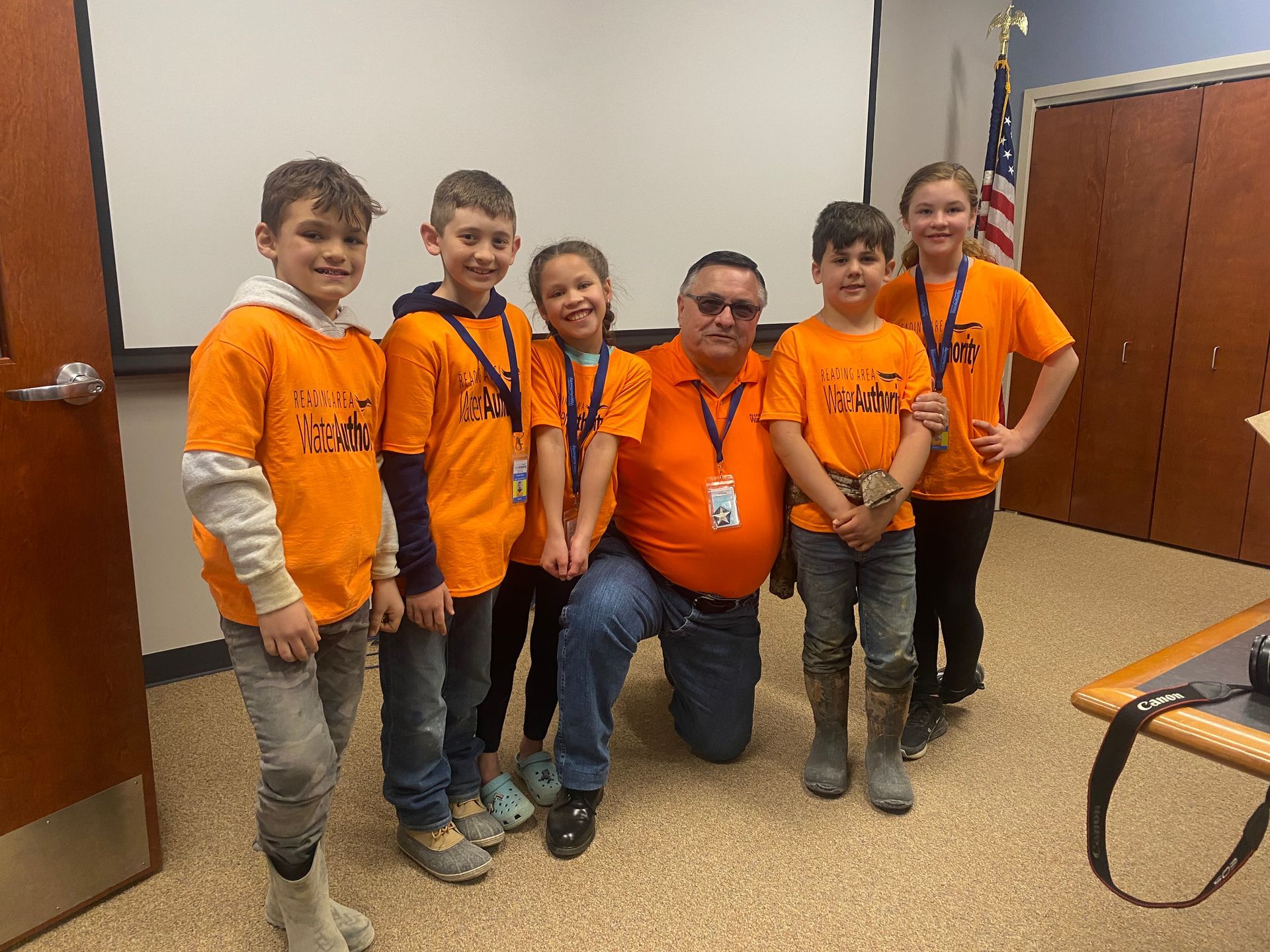 Group of children and an adult in orange shirts posing for a photo.