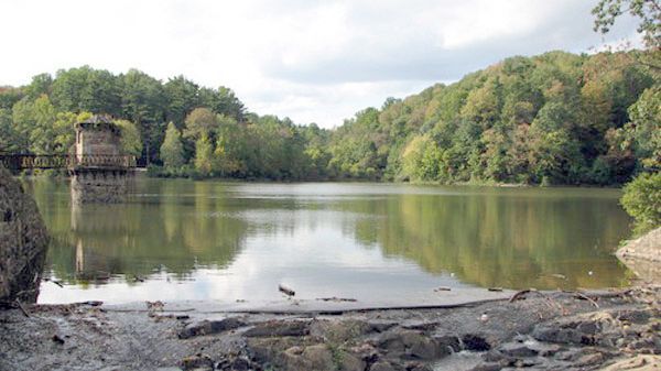 Still lake surrounded by green trees, with a stone structure on the left side.