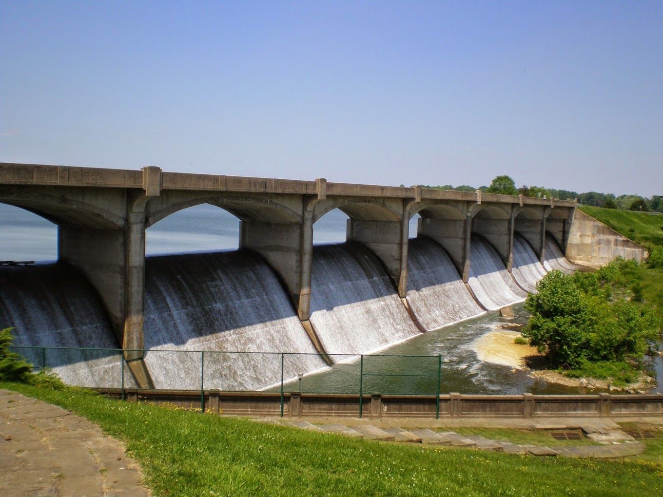 Concrete dam with water cascading over a curved spillway under a clear blue sky.
