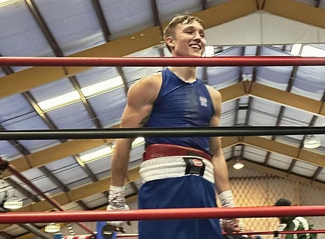 Boxer in a blue singlet and shorts smiles in the boxing ring.
