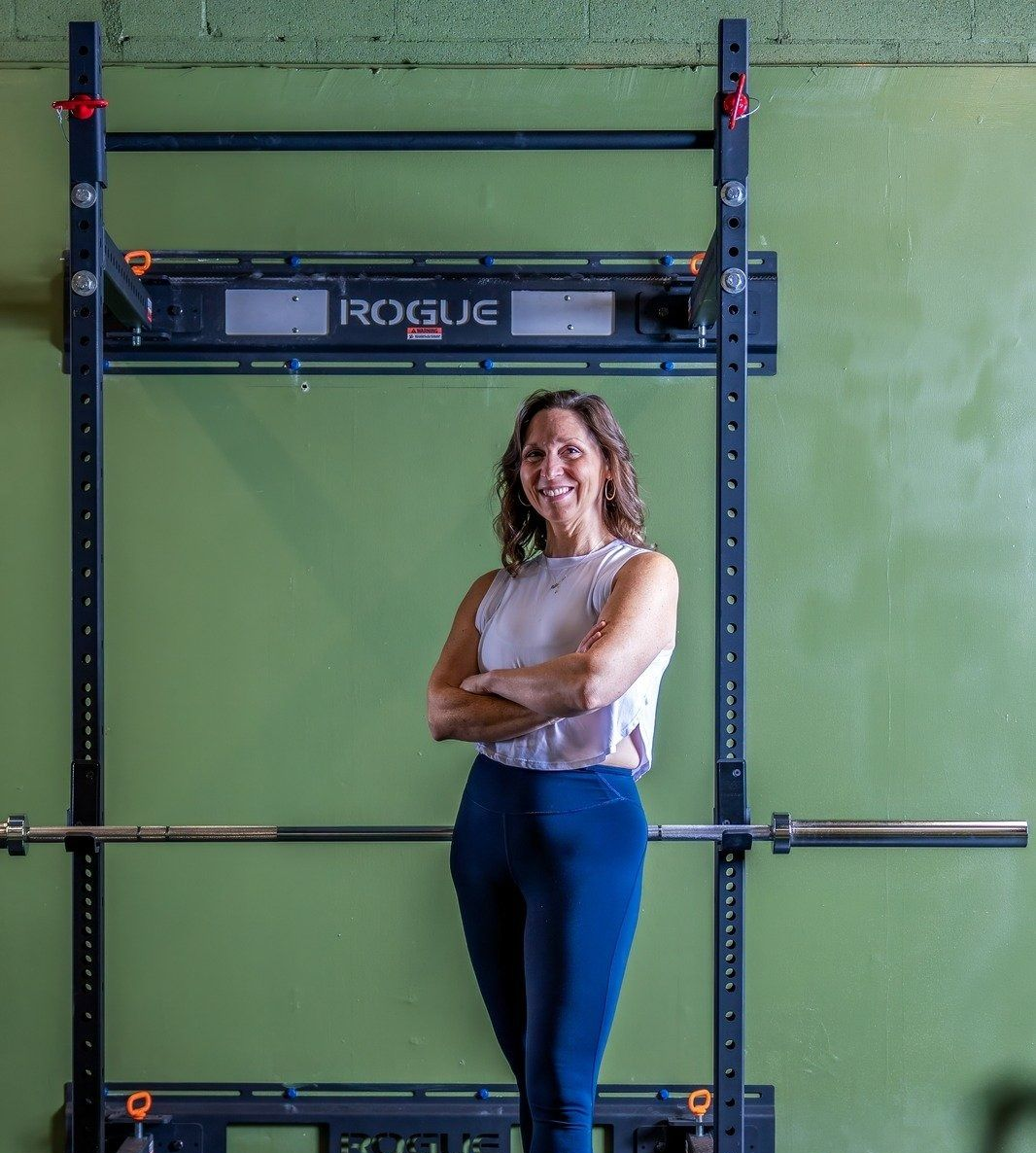 Man shirtless, exercising with a sledgehammer in a gym, chest tattoo, serious expression.