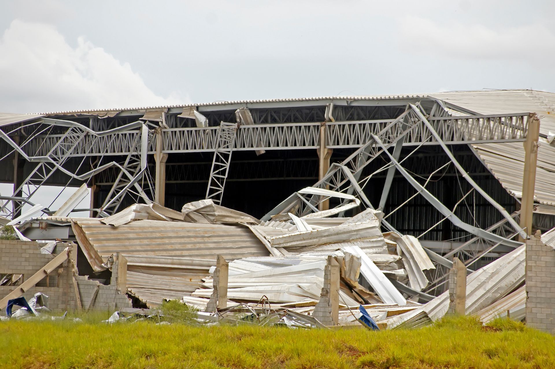 Destroyed building with collapsed roof and scattered debris on a grassy field.