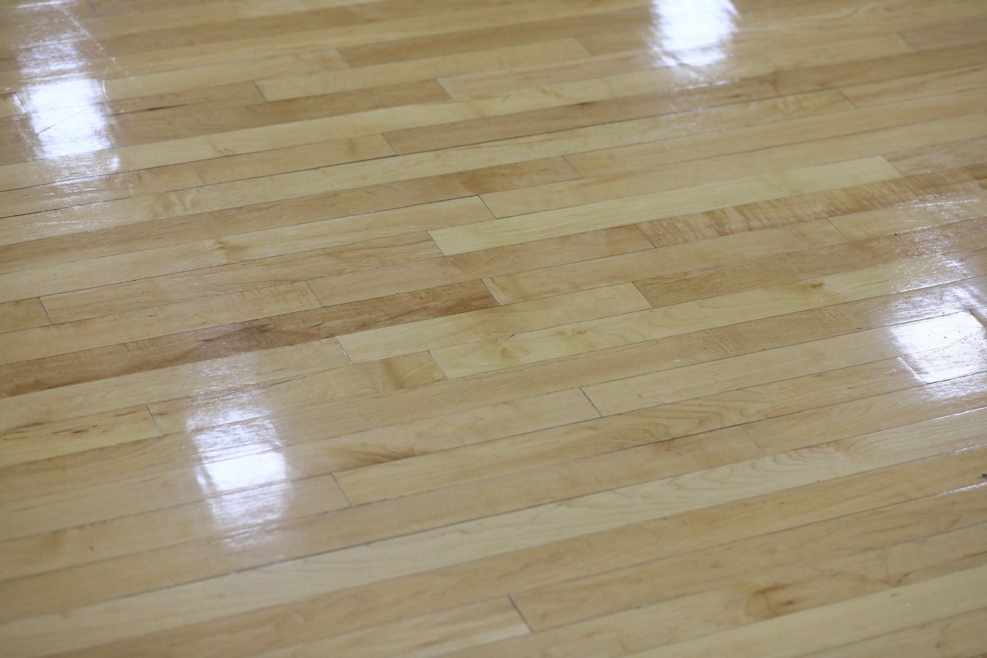 Close-up of shiny, light-colored wooden floor with horizontal planks reflecting bright light.