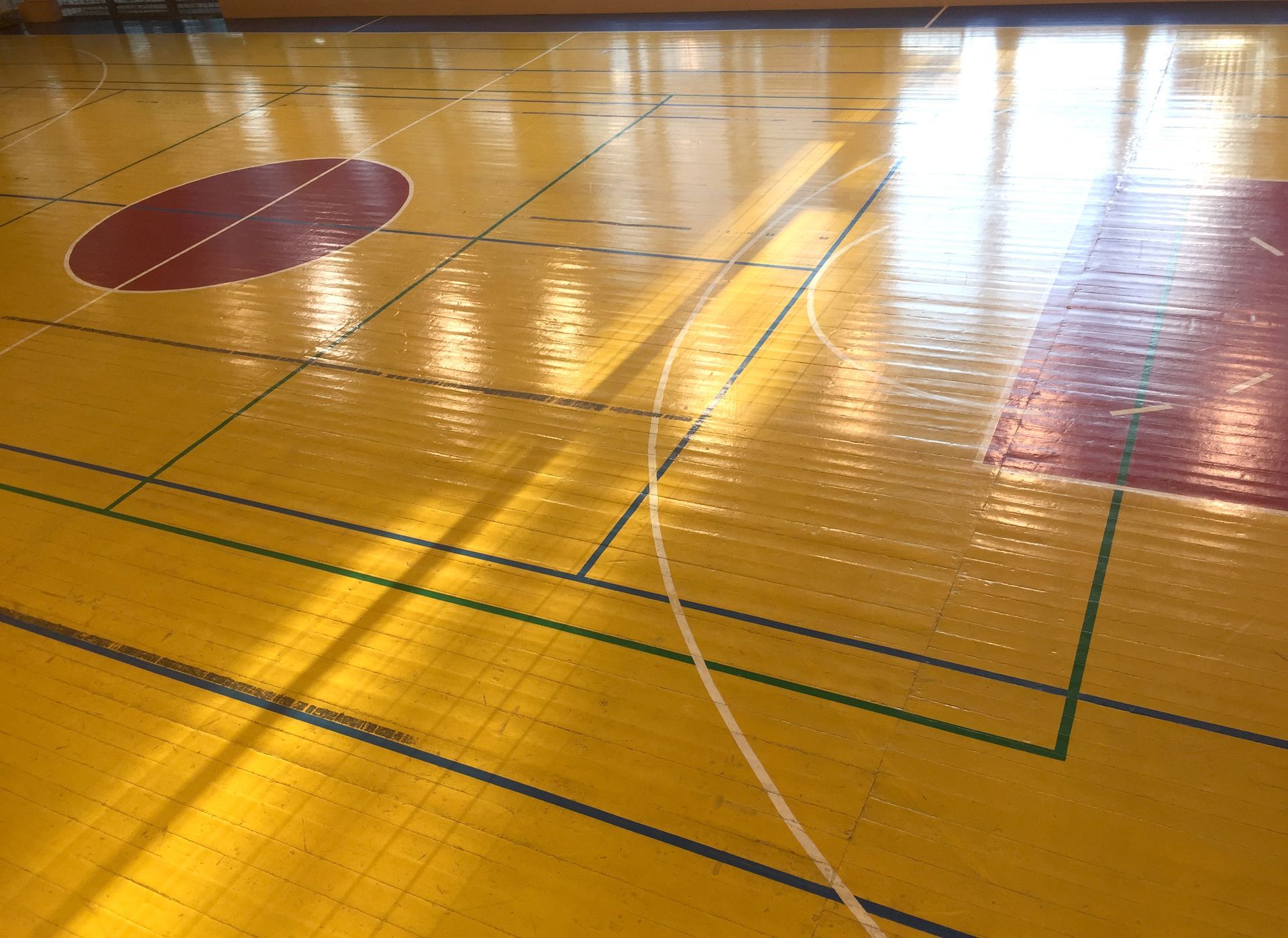 Yellow basketball court with red circles and lines, sunlight reflecting.