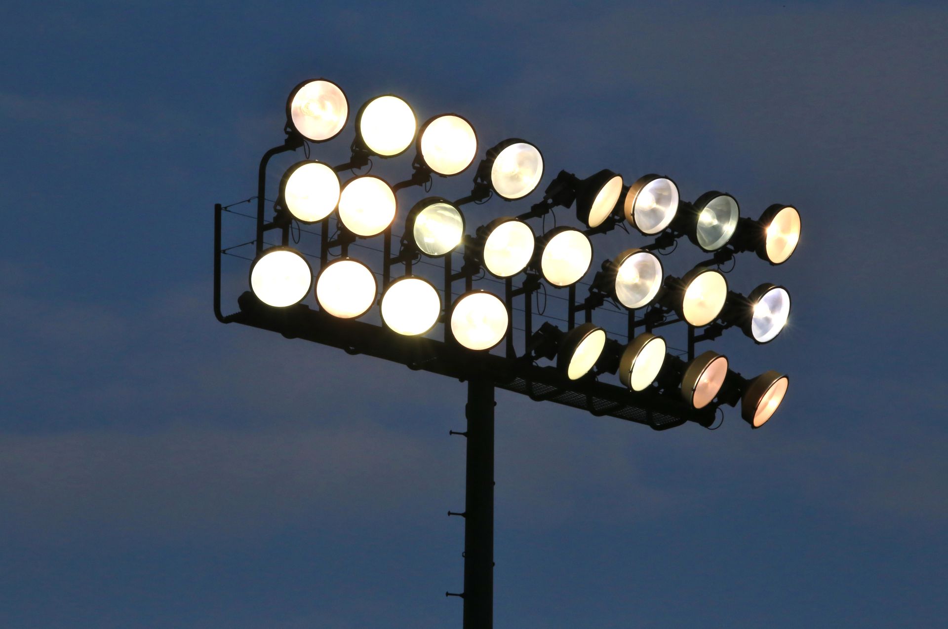 Stadium lights against a dark blue sky. Bright, round lights on a tall pole.