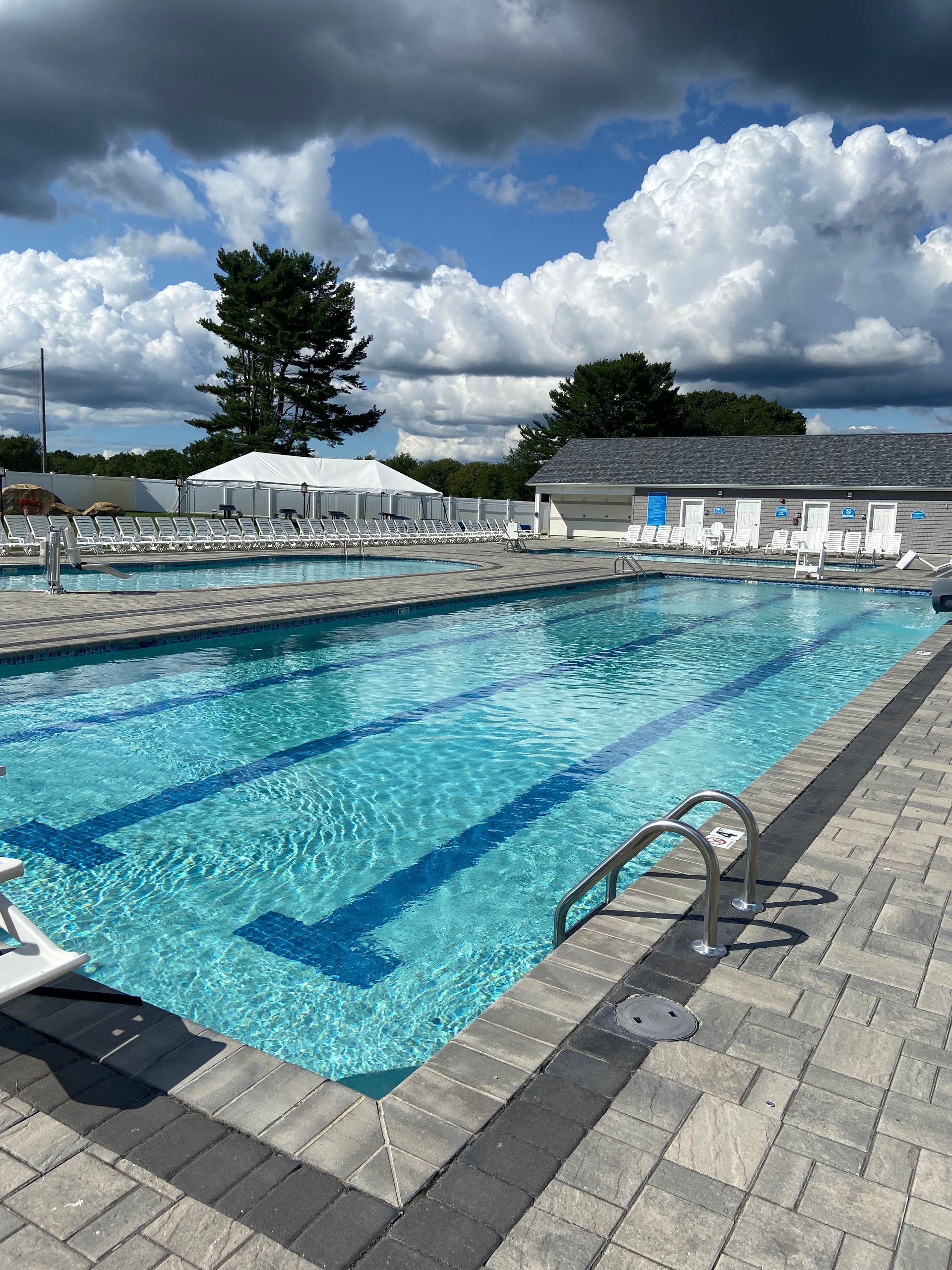 A large swimming pool surrounded by chairs and umbrellas on a cloudy day.