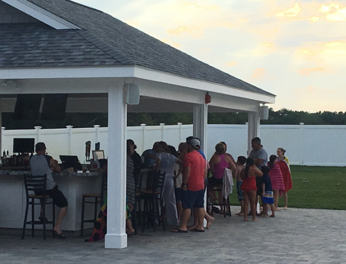 A group of people standing around a bar under a pavilion