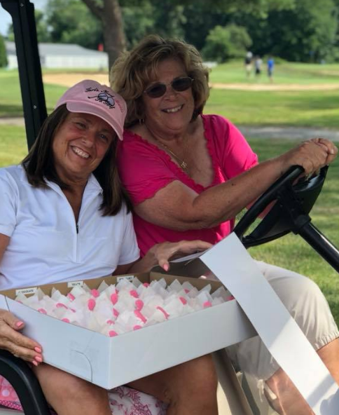 Two women are sitting in a golf cart and one is holding a box