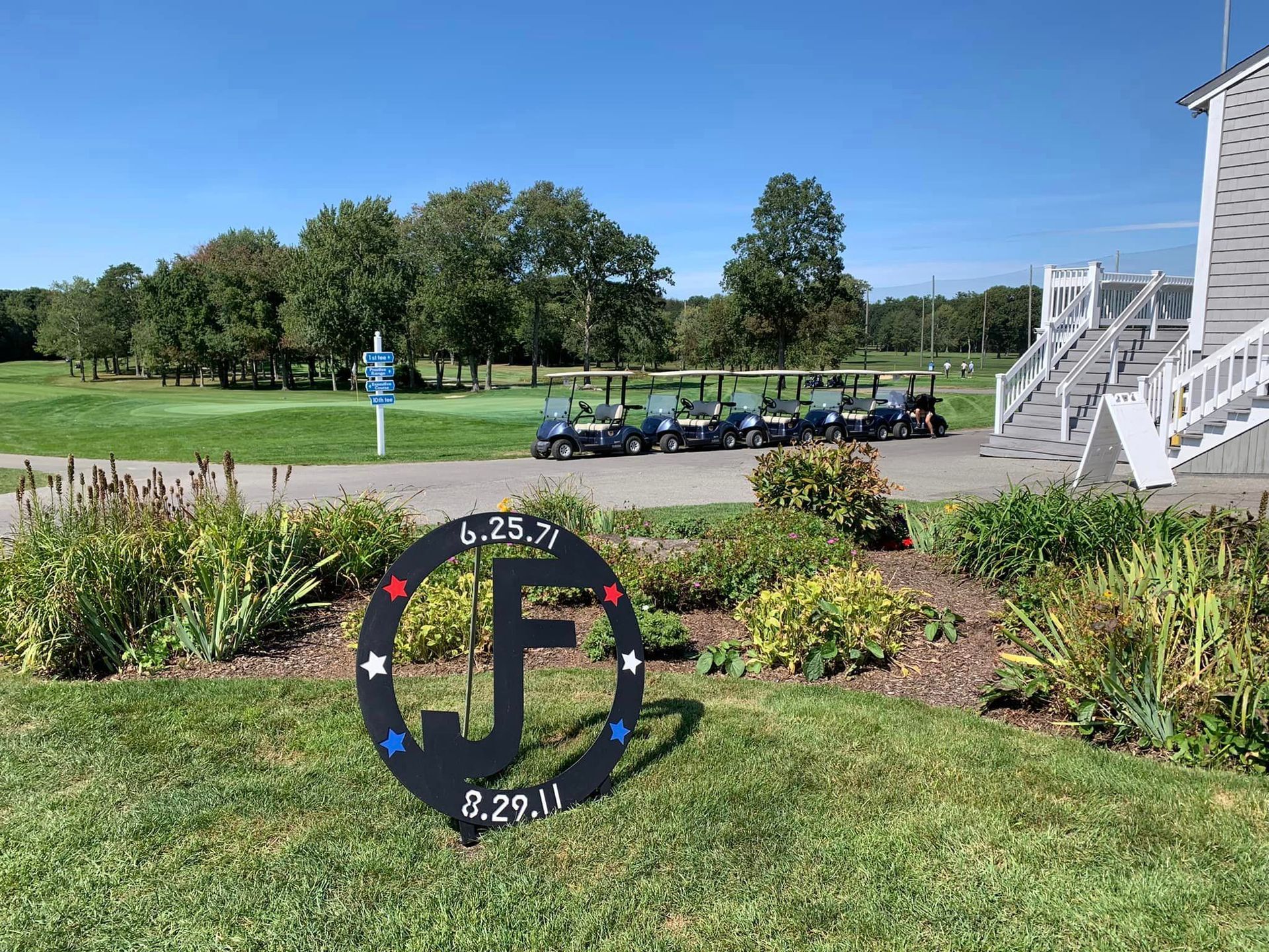 A sign that says `` jf '' is sitting in the grass in front of a golf course.